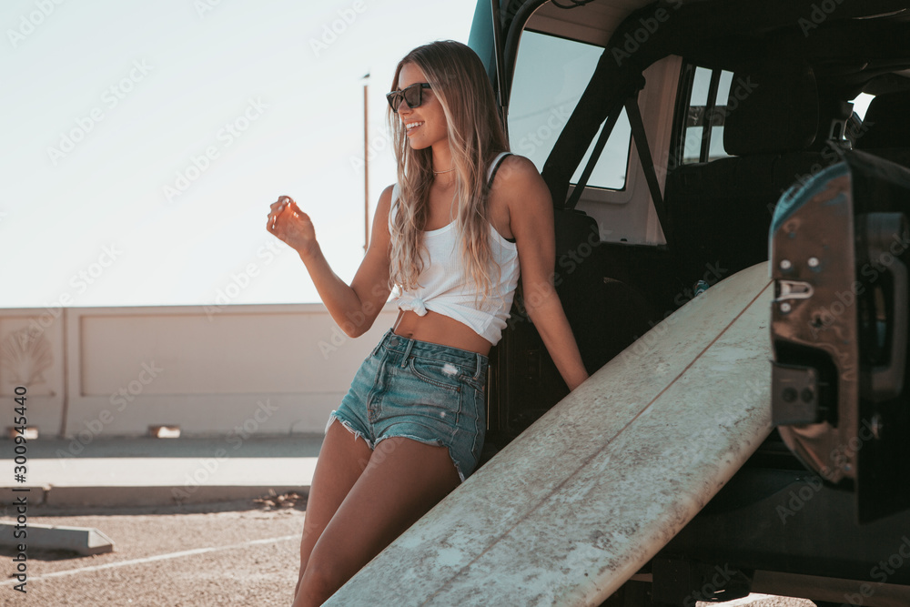 surfer girl sitting at a car with surfboard. california lifestyle - obrazy, fototapety, plakaty 