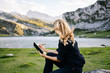© Dani - A beautiful caucasian blonde woman writes and draws on a notepad in a mountain landscape with lake