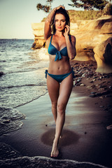 Wall Mural - Beautiful brunette girl in bikini posing on a beach