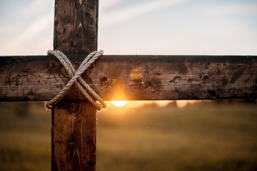 closeup shot of a wooden cross with the sun in the blurred background