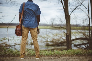 Closeup shot from behind of a male standing near a lake while holding the bible