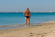 © Alexey - an elderly man standing on the sand sunbathes on the sea beach of the resort