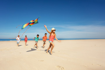 Canvas Print - Girl run with kite and group of kids on the beach