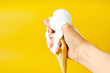 Creamy ice cream melted in the hands on a yellow background. The ice cream cone began to melt running down the arm.