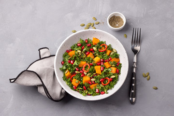 Plate of kale salad, baked pumpkin, pumpkin seeds and pomegranate on gray background, top view. healthy diet food