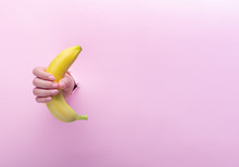 A Woman Holds A Banana In Her Hand, Inserted Through A Hole In Torn Paper