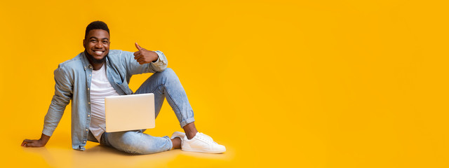 African man sitting with laptop on floot, gesturing thumb up