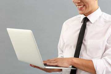 Asian businessman with laptop on grey background