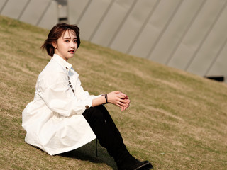 Beautiful young brunette woman in white shirt sitting and smiling at camera in sunny day. Outdoor fashion portrait of glamour Chinese cheerful stylish girl, emotions, beauty and lifestyle concept.