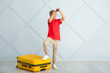 Poster - Cute little boy with suitcase and spyglass near light wall