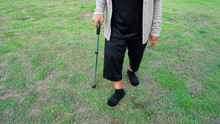 Senior Woman Legs Walking With Walking Stick In Grass Field