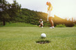 © Pop Sujinun - Golfer putting golf ball on the green golf, lens flare on sun set evening time.
