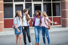 Candid Photo Of A Group Of Teenage Girls Socializing, Laughing And Talking Together At School. A Multi-ethnic Group Of Real Junior High Aged Students Walking Outside A School Building
