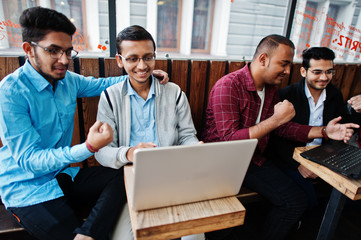 Group of four indian teen male students. Classmates spend time together and work at laptops.