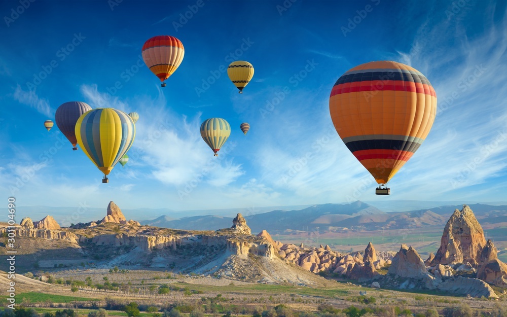 Colorful hot air balloons fly in blue sky over amazing valleys with fairy chimneys in Cappadocia, Turkey - obrazy, fototapety, plakaty 