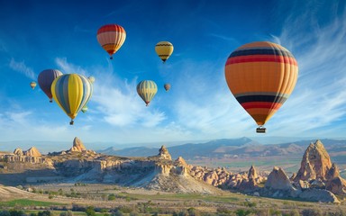 colorful hot air balloons fly in blue sky over amazing valleys with fairy chimneys in cappadocia, tu