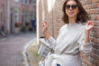 © papa - A happy young woman in sunglasses stands on a city street, leaning against a brick wall.Modern street fashion in the summer season.