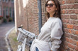 © papa - A happy young woman in sunglasses stands on a city street, leaning against a brick wall.Modern street fashion in the summer season.