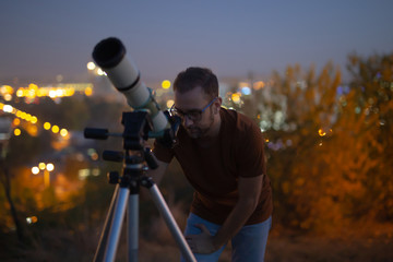 Wall Mural - astronomer with a telescope watching at the stars and moon with blurred city lights in the backgroun