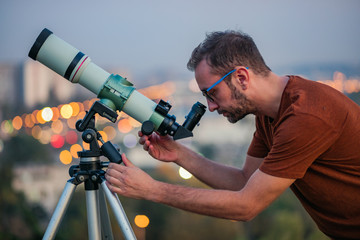 Wall Mural - astronomer with a telescope watching at the stars and moon with blurred city lights in the backgroun