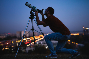 Wall Mural - astronomer with a telescope watching at the stars and moon with blurred city lights in the backgroun