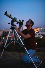Wall Mural - astronomer with a telescope watching at the stars and moon with blurred city lights in the backgroun