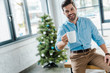 © LIGHTFIELD STUDIOS - selective focus of happy bearded man holding cup with coffee near christmas tree in office