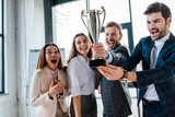 Fototapeta  - selective focus of excited multicultural businesswomen and businessmen looking at trophy in office