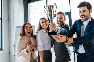 Wall Mural - selective focus of excited multicultural businesswomen and businessmen looking at trophy in office