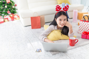 attractive asian female shopping with online market in Christmas celebration seasonal, she rest face on hand and stay on floor, she search and play internet with laptop, she feeling happy and smile