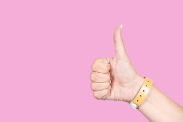 Close up side view of beautiful one female hand isolated on pink background. Woman showing thumb up, wrist with rubber orange entrance bracelet. Horizontal color photography.