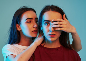 Let's keep it a secret. Studio shot indoors with neon light. Photo of two beautiful twins