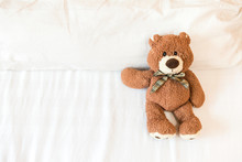 Fluffy Brown Teddy Bear Lying Down On The Bed Alone With Space On White Bed Sheet