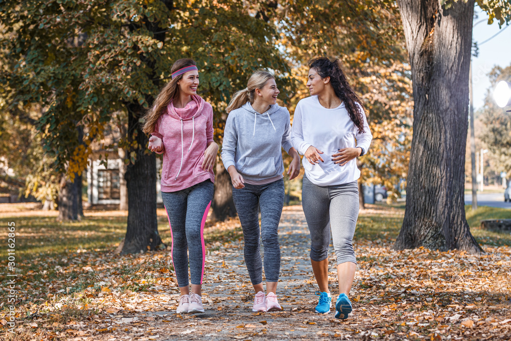 up of female friends jogging at the city park.Relaxing after running and making fun.Autumn season.	 - obrazy, fototapety, plakaty 