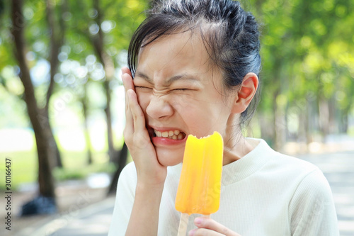 Asian child girl having hypersensitive teeth eating ice-pop,feel painful,female teenage have sensitive teeth with ice-lolly,sad woman suffer toothache and tooth decay,dental care,health care concept