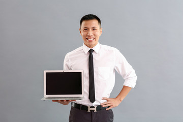 Wall Mural - Asian businessman with laptop on grey background