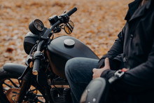 Cropped Shot Of Faceless Biker Poses On Fast Motorbike, Stops In Park, Ground Covered With Fallen Leaves, Enjoys Travel And Journey. People, Lifestyle, Transport Concept.