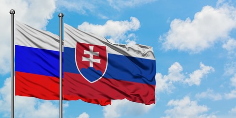 Russia and Slovakia flag waving in the wind against white cloudy blue sky together. Diplomacy concept, international relations.