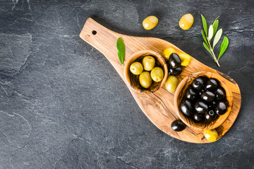 Wall Mural - Fresh green and black fresh olives on dark stone table top view. Olive leaves and picker on rustic board.