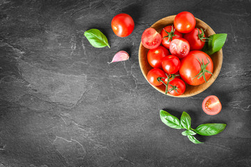 Wall Mural - Fresh red tomatoes in wooden bowl on dark stone table or black background. Beautiful tomato and basil top view with copy space.