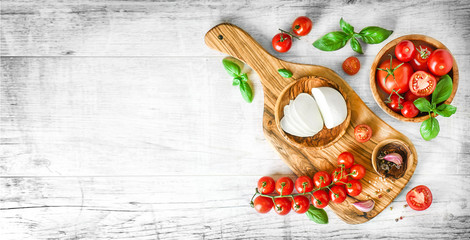 Wall Mural - Mozzarella cheese and fresh tomatoes with basil on white table, top view. Beautiful red tomato vegetables concept with copy space, banner or panorama.