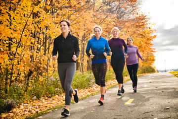 woman group out running together in an autumn park they run a race or train in a healthy outdoors lifestyle concept