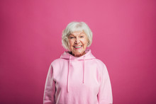 Happy Cheerful Positive Old Woman Smiling Wide And Look Straight On Camera. Stand Straight. Modern Stylish Senior Model With Grey Hair. Isolated Over Pink Background.