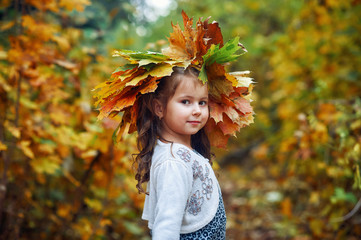 Portrait of a little girl in the autumn Park, a girl with a wreath of maple leaves .