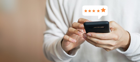 close up on customer man hand pressing on smartphone screen with gold five star rating feedback icon