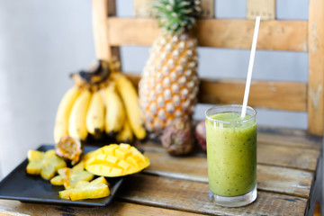 Tasty bananas, carambola with pine apple and mango on wooden chair, green fresh kiwi juice.