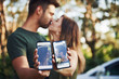 © standret - Holding two smartphones with photos of them. Beautiful young couple have a good time in the forest at daytime