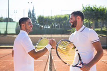 Side View Of Two Tennis Players With Rackets Shaking Hands And Smiling Before Tennis Match