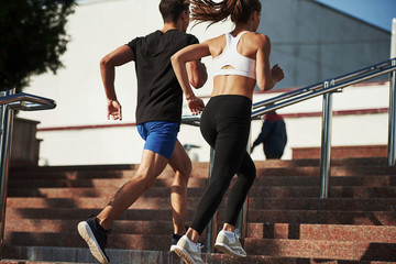 On the stairs. Man and woman have fitness day and running in the city at daytime