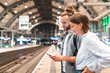 © WILLIAM PERUGINI/Westend61 - Young couple waiting for the train at the station and using smartphone, Berlin, Germany